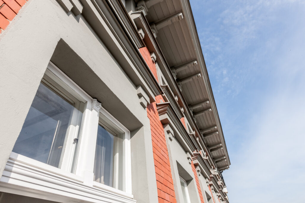 Detailaufnahme der grauen Fassade mit Fenster und blauem Himmel.